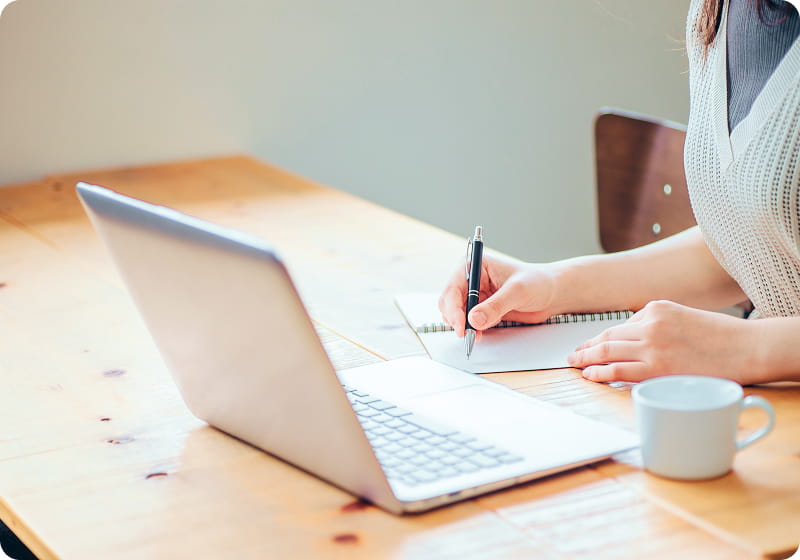パソコンとノートを使って作業している女性の手元